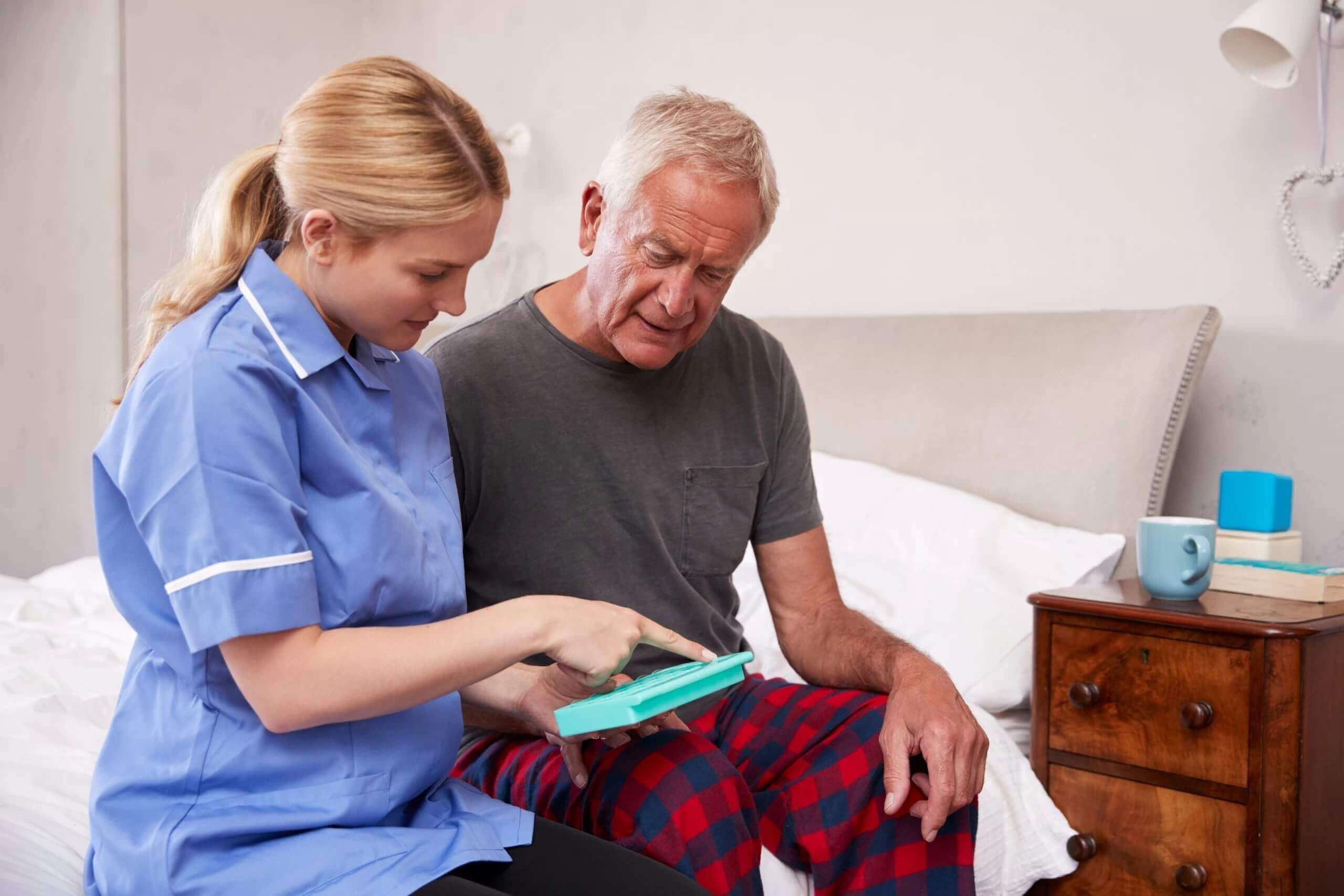 An elderly man sitting with a nurse looking at a box of tablets